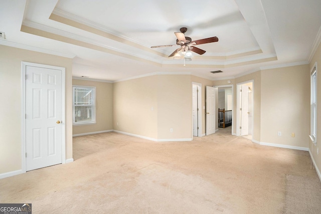 empty room with a raised ceiling, light colored carpet, visible vents, and baseboards