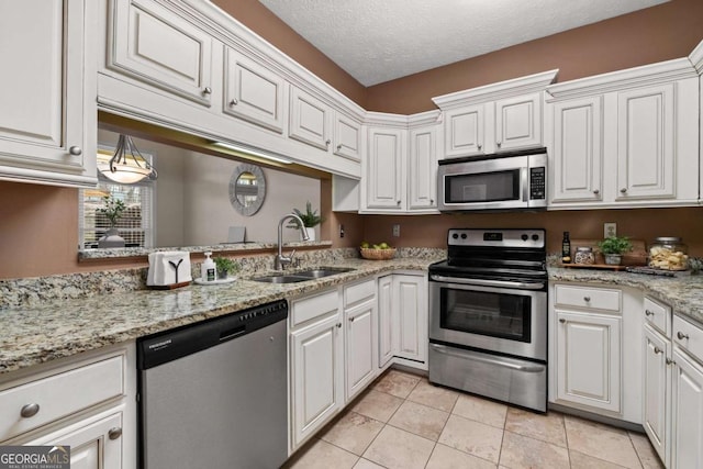 kitchen with light tile patterned floors, white cabinets, stainless steel appliances, a textured ceiling, and a sink