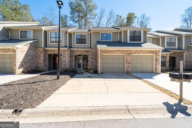 townhome / multi-family property with driveway, brick siding, an attached garage, and a shingled roof