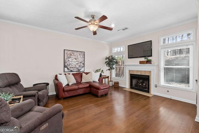 living room featuring a tile fireplace, visible vents, crown molding, and wood finished floors