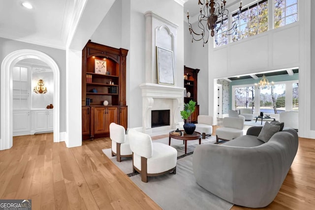 living area with a high end fireplace, built in features, light wood-style flooring, an inviting chandelier, and arched walkways