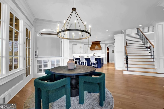 dining area with light wood-style flooring, arched walkways, stairs, crown molding, and a notable chandelier