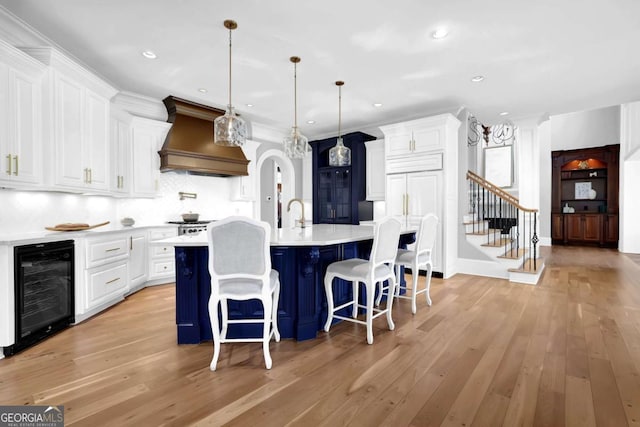 kitchen featuring beverage cooler, light countertops, custom range hood, arched walkways, and white cabinetry