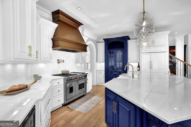 kitchen with light wood-type flooring, custom range hood, range with two ovens, white cabinetry, and a sink