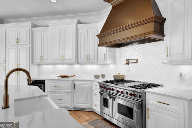 kitchen featuring custom exhaust hood, range with two ovens, white cabinets, and a sink