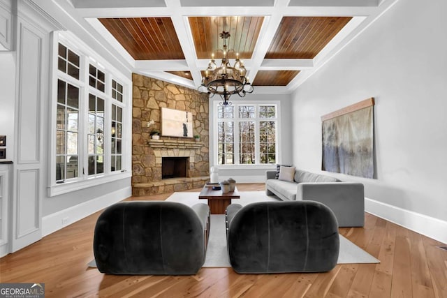 living area with a stone fireplace, a notable chandelier, baseboards, and hardwood / wood-style floors