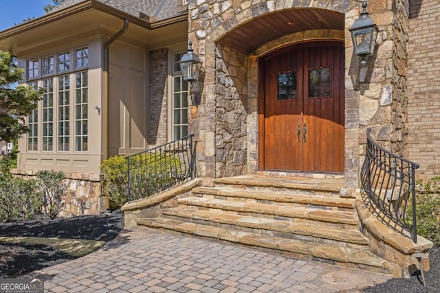 view of exterior entry with stone siding, brick siding, and a shingled roof