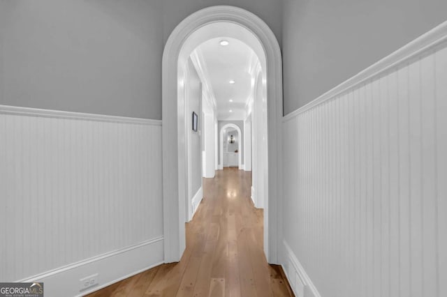 corridor with arched walkways, a wainscoted wall, and wood finished floors