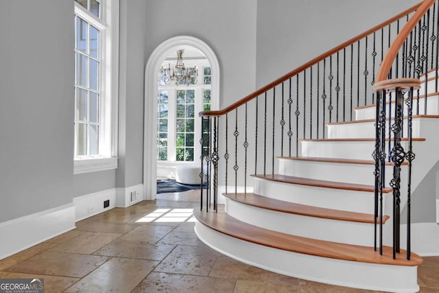 entrance foyer with stone tile floors, a chandelier, baseboards, a towering ceiling, and stairs