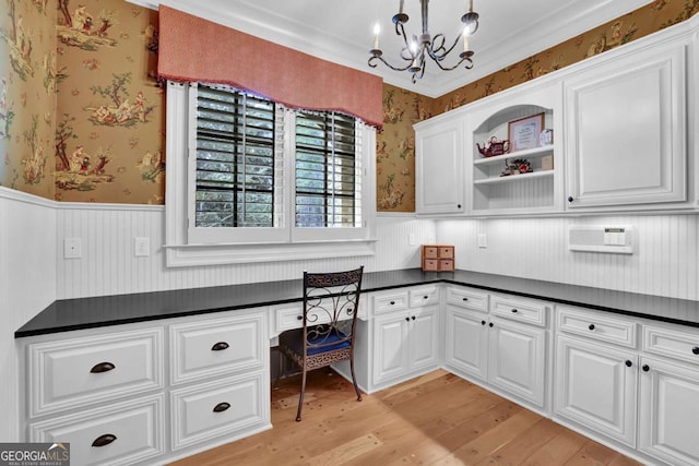 home office with light wood finished floors, built in desk, wainscoting, and wallpapered walls