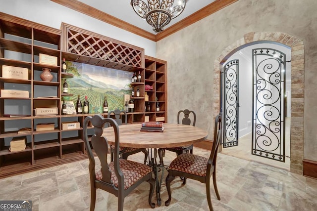 wine area featuring arched walkways, an inviting chandelier, crown molding, and stone finish floor