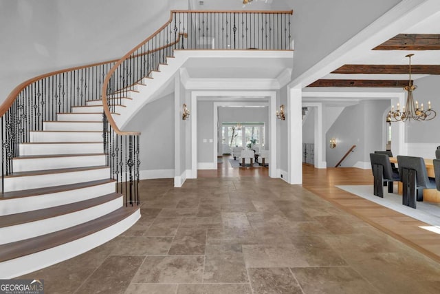 foyer featuring stone finish flooring, baseboards, stairs, a high ceiling, and an inviting chandelier