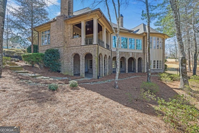 view of front of house with a balcony, fence, stone siding, and a chimney