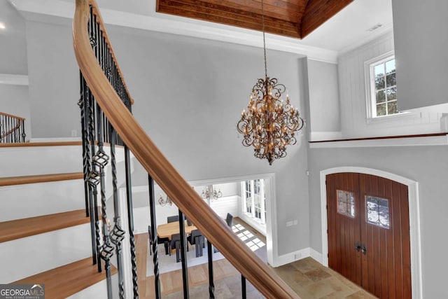 foyer featuring baseboards, stairs, a high ceiling, an inviting chandelier, and a raised ceiling