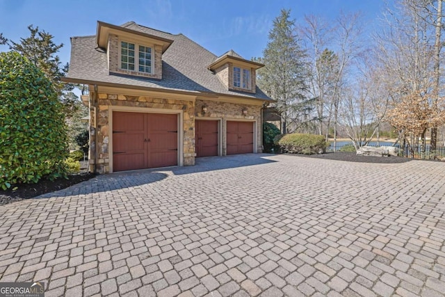 view of front of home with decorative driveway, stone siding, roof with shingles, and an attached garage