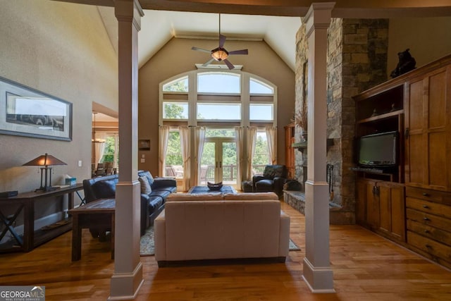 living area featuring high vaulted ceiling, a stone fireplace, light wood-type flooring, and decorative columns