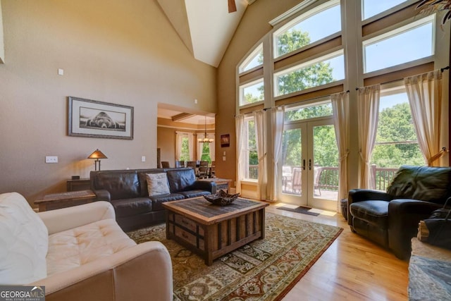 living room with light wood-type flooring, plenty of natural light, high vaulted ceiling, and french doors