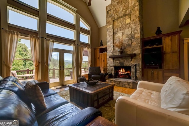 living room with a stone fireplace, french doors, high vaulted ceiling, and wood finished floors