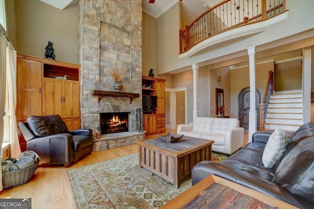 living area featuring a high ceiling, a fireplace, wood finished floors, stairway, and decorative columns