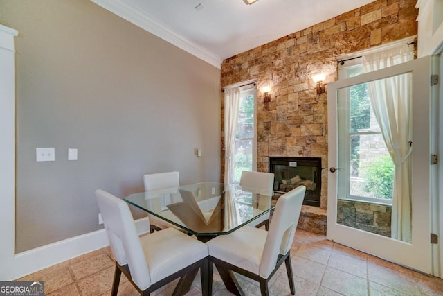 dining space with baseboards, a stone fireplace, ornamental molding, and a healthy amount of sunlight