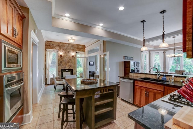 kitchen with stainless steel appliances, a sink, ornamental molding, brown cabinetry, and decorative light fixtures