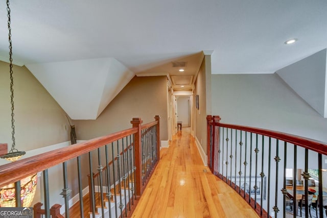 corridor with vaulted ceiling, visible vents, wood finished floors, and an upstairs landing