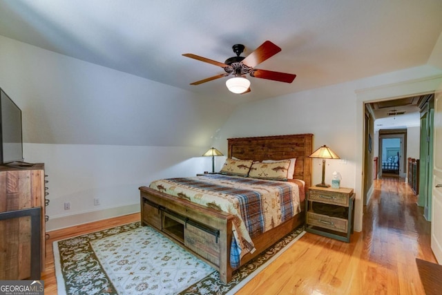 bedroom featuring lofted ceiling, attic access, baseboards, and wood finished floors