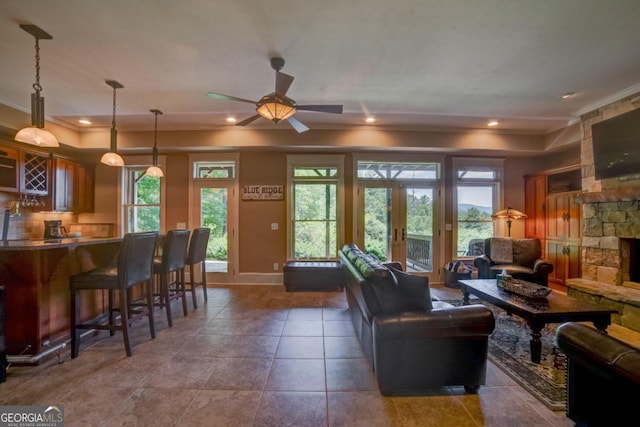 living area featuring french doors, ornamental molding, a stone fireplace, bar area, and dark tile patterned floors