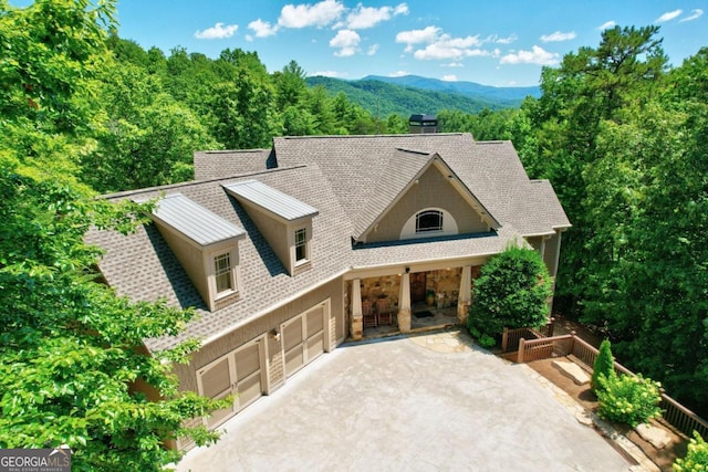 view of front of property featuring roof with shingles, an attached garage, a mountain view, driveway, and a forest view