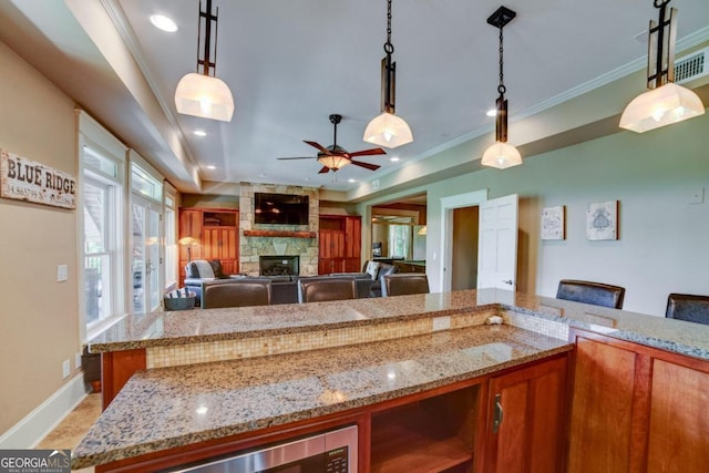 kitchen with light stone counters, brown cabinets, hanging light fixtures, crown molding, and a stone fireplace