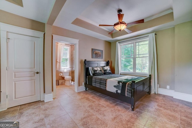 bedroom with a tray ceiling, crown molding, baseboards, and ensuite bathroom