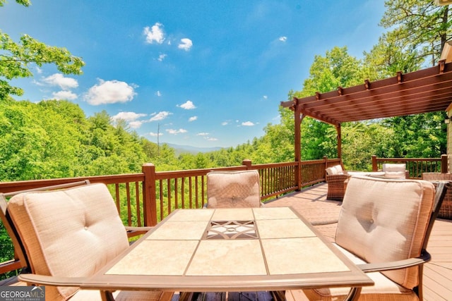 wooden terrace with outdoor dining space, a wooded view, and a pergola