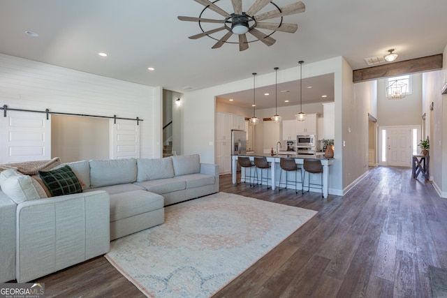 living room with a ceiling fan, a barn door, baseboards, and dark wood-type flooring