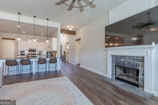 kitchen featuring a stone fireplace, a breakfast bar, a ceiling fan, white cabinets, and stainless steel microwave