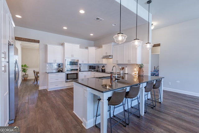 kitchen with dark countertops, visible vents, appliances with stainless steel finishes, a sink, and a peninsula