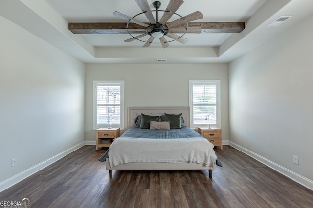 bedroom with dark wood-style floors, a tray ceiling, visible vents, and baseboards