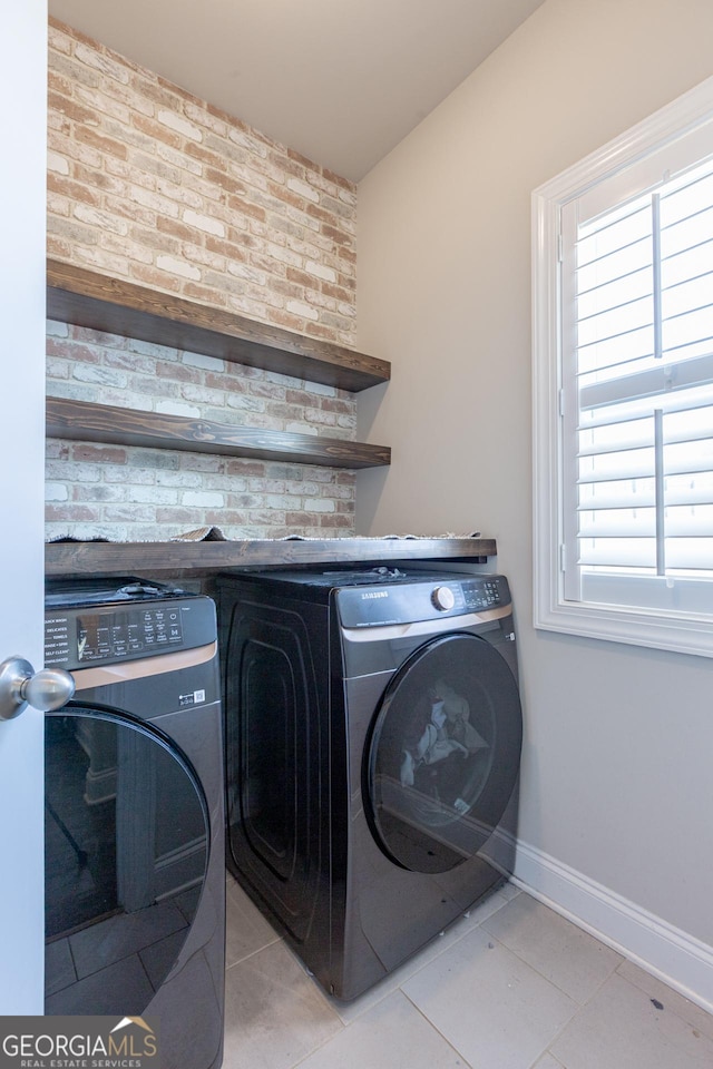 washroom featuring laundry area, light tile patterned floors, baseboards, brick wall, and washing machine and clothes dryer