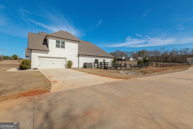 view of home's exterior with concrete driveway, roof with shingles, fence, and an attached garage