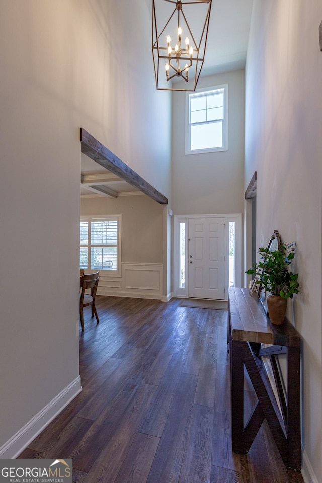 foyer entrance with dark wood-style flooring, a wainscoted wall, a decorative wall, an inviting chandelier, and baseboards