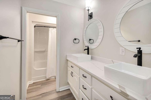 full bathroom featuring double vanity, a shower with shower curtain, a sink, and wood finished floors