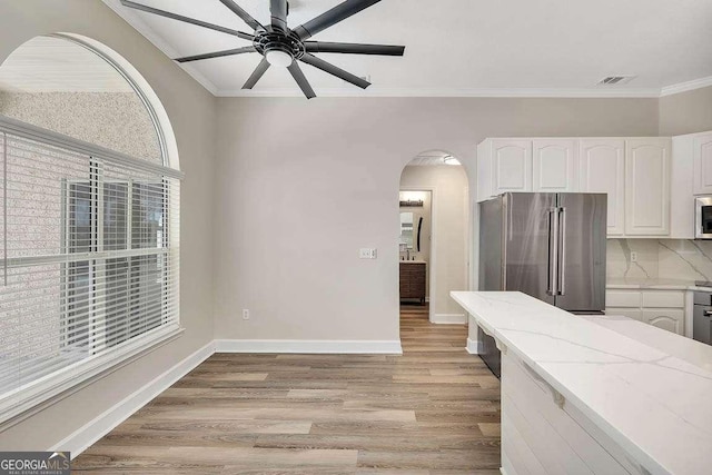 kitchen with light stone counters, high end refrigerator, white cabinetry, ornamental molding, and light wood-type flooring