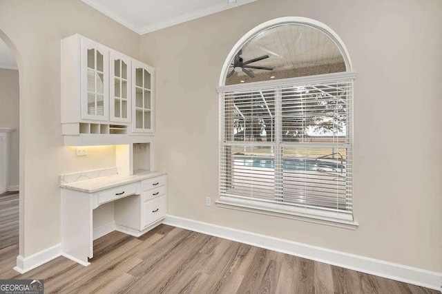 unfurnished office featuring light wood-type flooring, arched walkways, crown molding, and baseboards