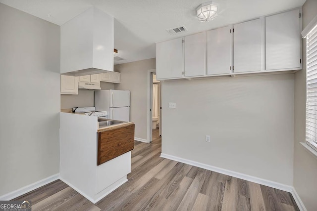 kitchen with white appliances, baseboards, visible vents, light wood-style floors, and under cabinet range hood