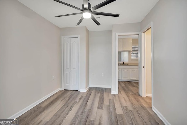 unfurnished bedroom featuring a closet, a ceiling fan, a sink, light wood-type flooring, and baseboards