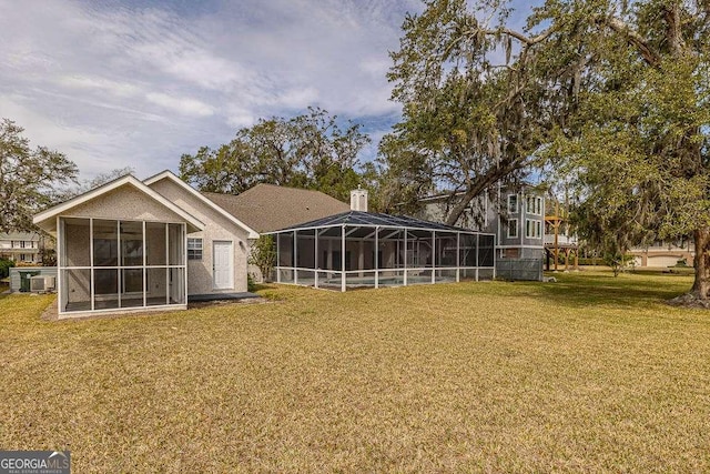 rear view of property with glass enclosure, a yard, and a chimney