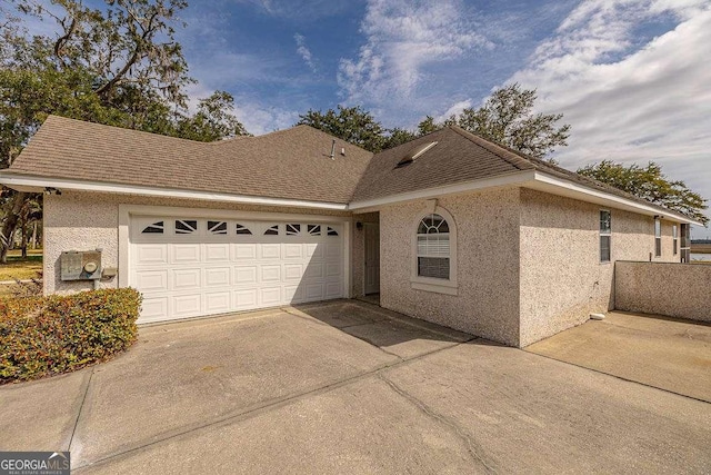 ranch-style house with driveway, roof with shingles, a garage, and stucco siding