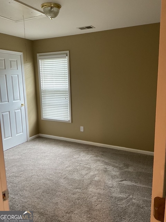 carpeted empty room featuring attic access, visible vents, and baseboards