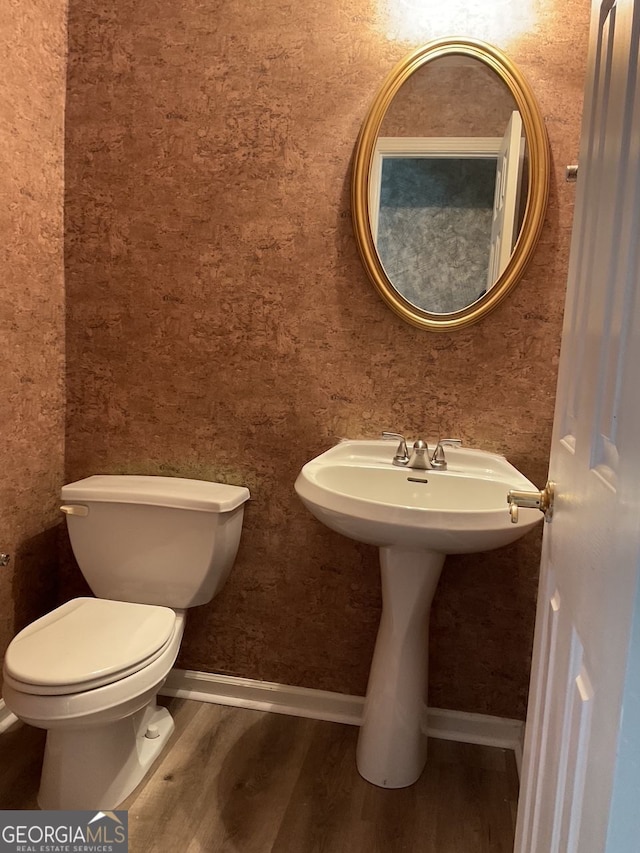 half bathroom featuring wood finished floors, toilet, and baseboards