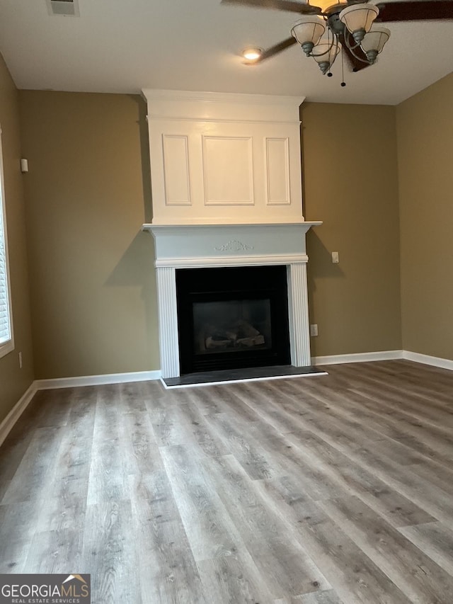 unfurnished living room featuring a ceiling fan, a glass covered fireplace, baseboards, and wood finished floors