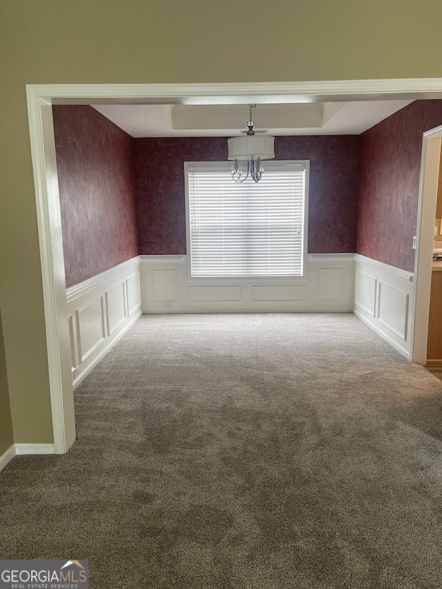 unfurnished dining area featuring wallpapered walls, a wainscoted wall, an inviting chandelier, carpet flooring, and a decorative wall